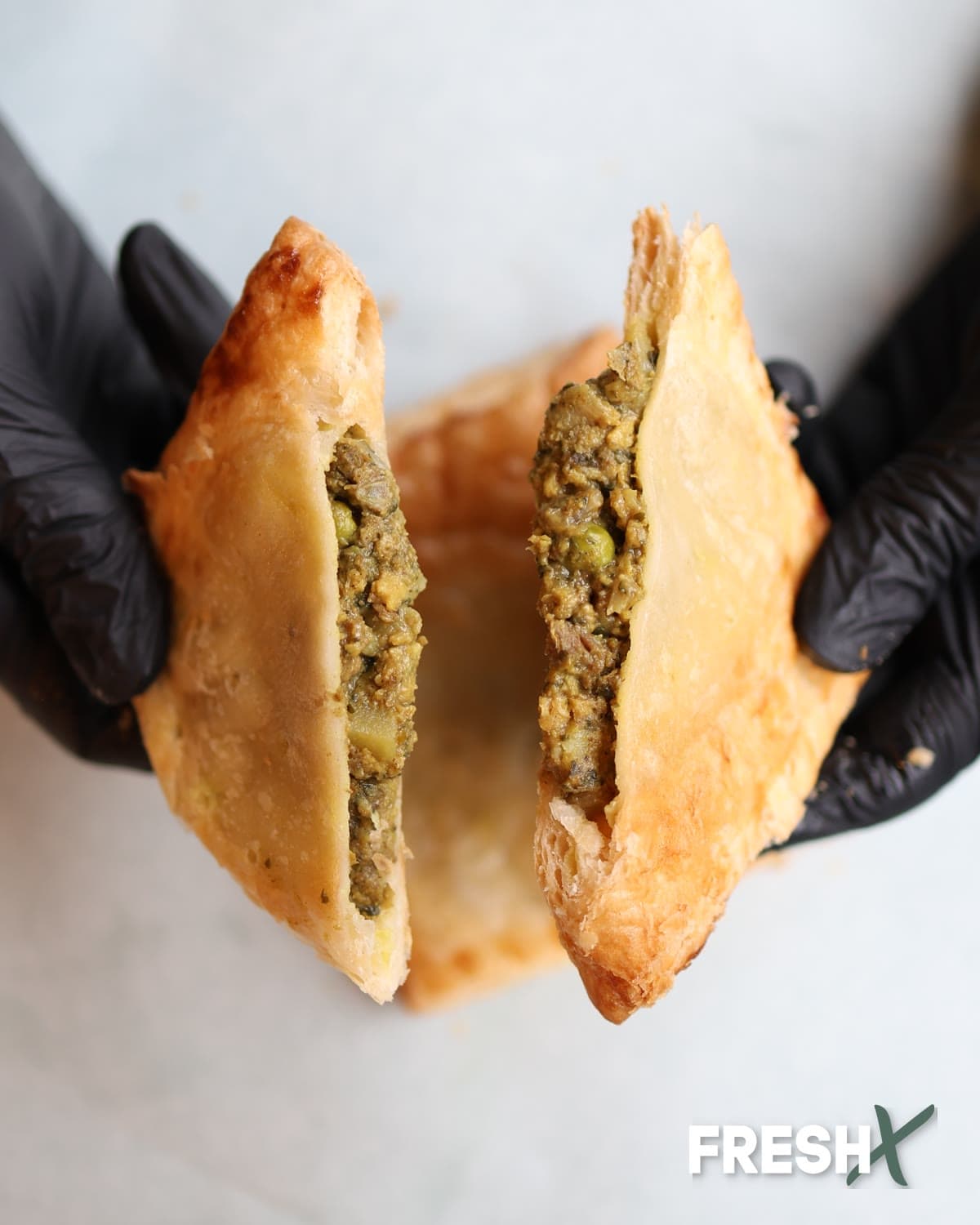 A golden flaky pastry pulled apart to show the filling