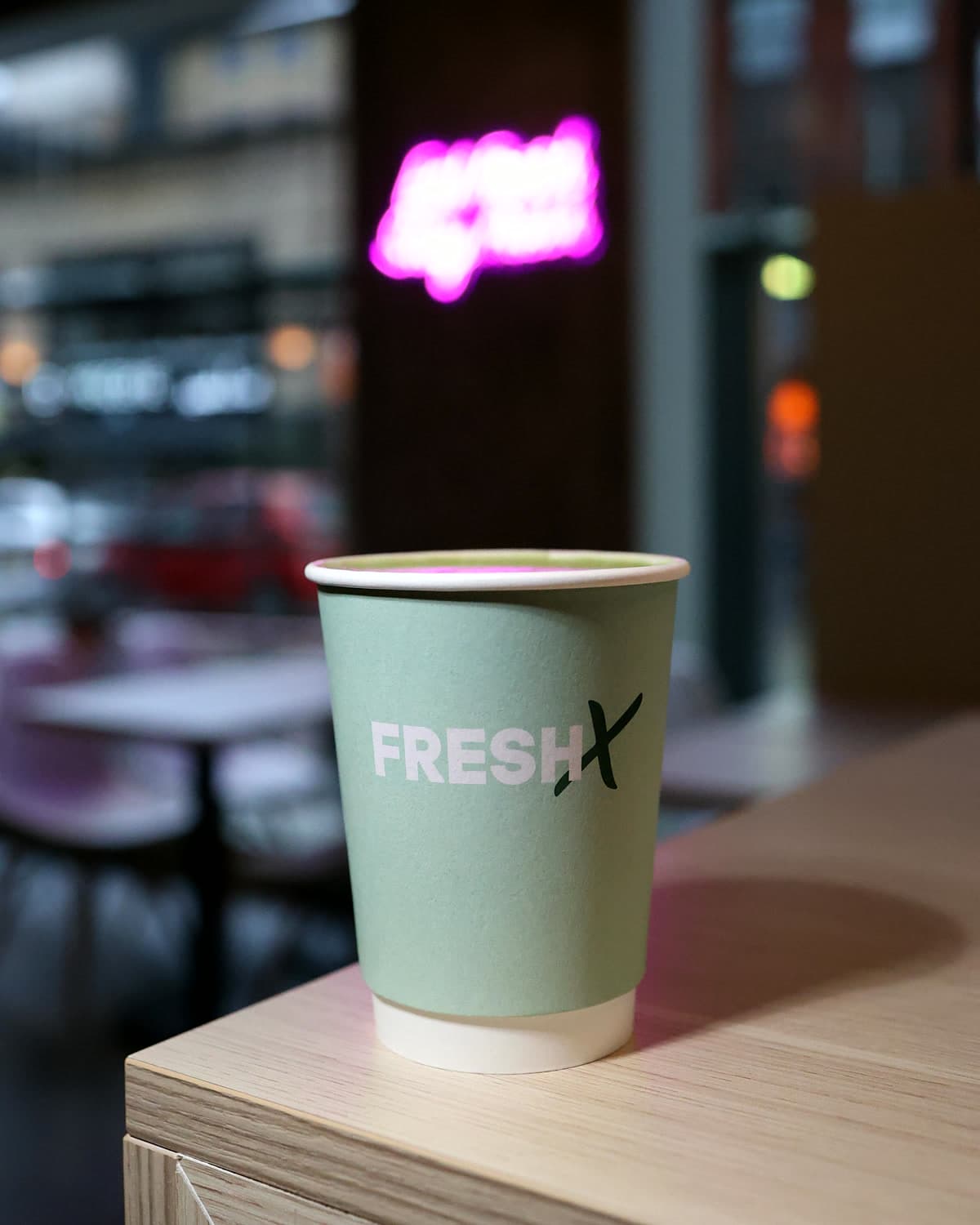 Sage FreshX cup on the counter edge with the pink neon sign glowing behind
