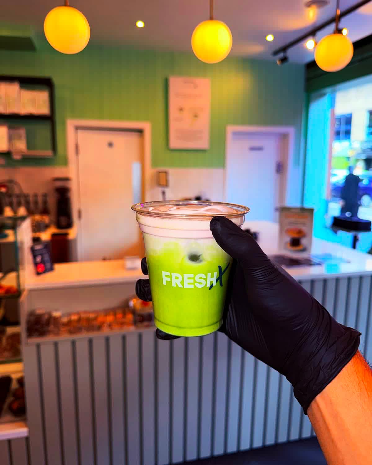 Iced matcha in a FreshX cup, held up inside the café